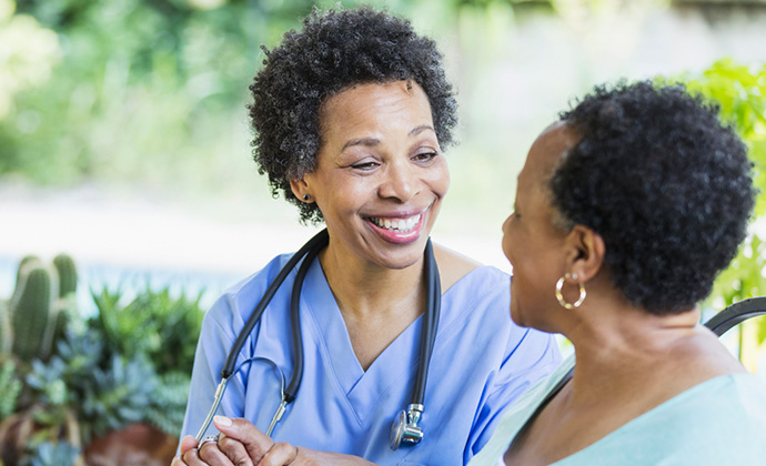 A Black nurse speaks with a senior Black patient.