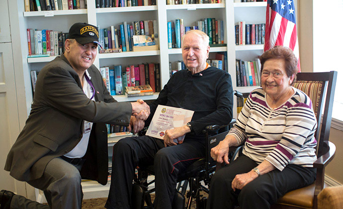 A VITAS team member shakes hands with a military veteran who is seated next to his spouse