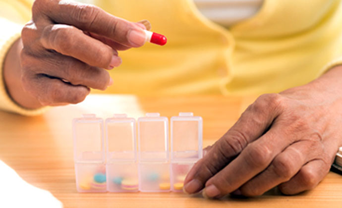 A senior citizen places a pill into a clear weekly pill box