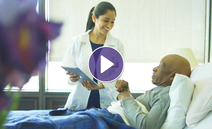 Una médica de VITAS usa una tablet mientras habla con un paciente que está en la cama de un hospital
