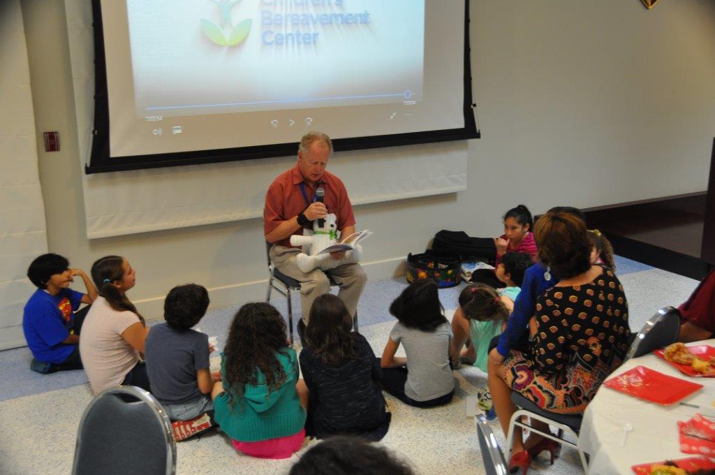 Children sit on the floor in a semicircle as an adult reads a book aloud