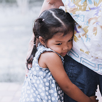 A grieving girl hugs an adult's leg