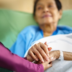 A caregiver holds the hand of a patient who is lying in bed