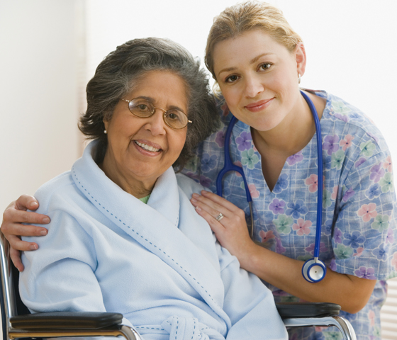 A patient in a wheelchair smiles with a nurse's assistant