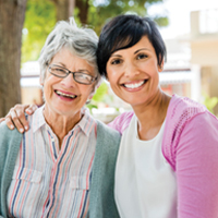 A chaplain and patient smile together outside beneath a tree