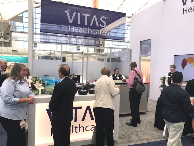 People talk with VITAS team members at the VITAS booth at a conference