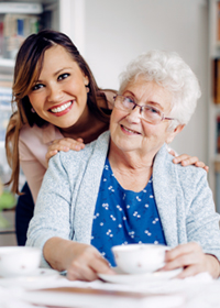 A female nursing assistant smiles with a female patient at a kitchen table