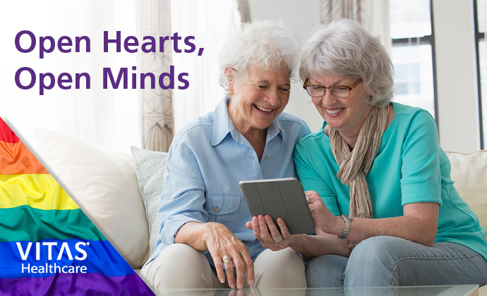 Two smiling, older woman sit together on a sofa and look at a tablet