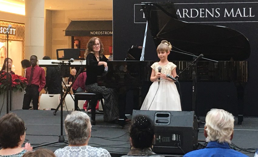 A girl in a white dress holds a microphone on stage