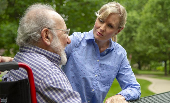 A woman enjoys a day outside with her older father, who is seated in a wheelchair