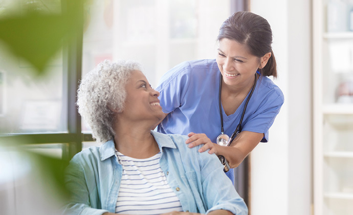 A nurse stands next to a woman and they smile at each other