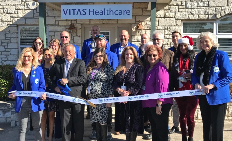 The group poses with ceremonial scissors and a large ribbon in front of the office