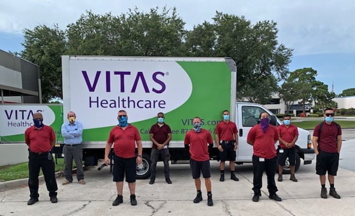 Nine members of the HME team wear their masks and stand in front of a delivery truck for a group photo