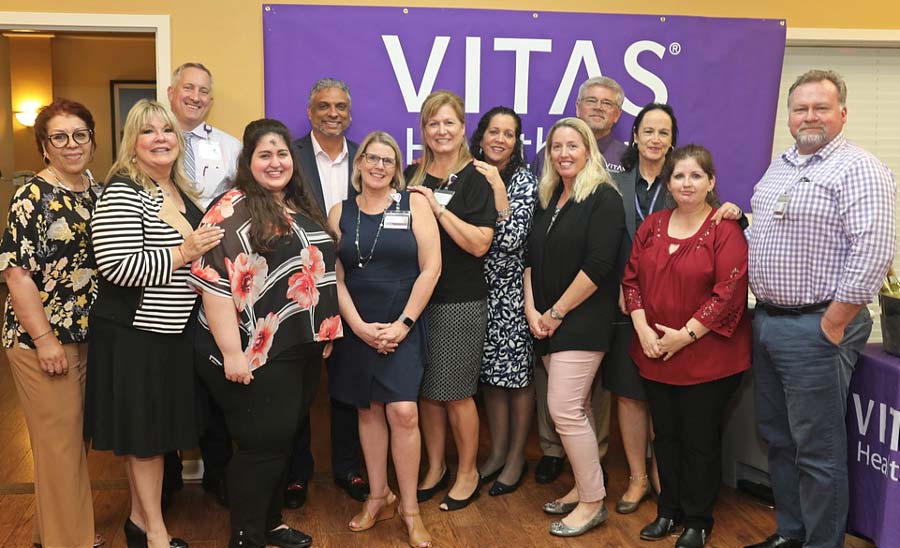 The VITAS team poses for a group photo at the open house in front of a purple VITAS banner