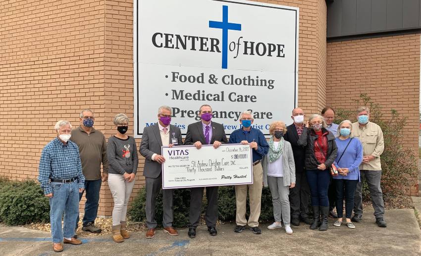 The team holds a large ceremonial check outside the Center of Hope