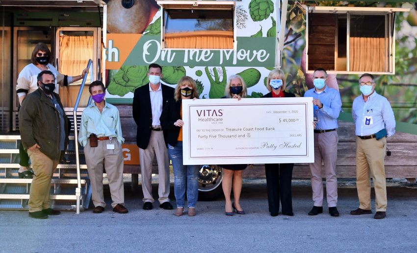 The group poses with a ceremonial check in front of the Treasure Coast Food Bank RV