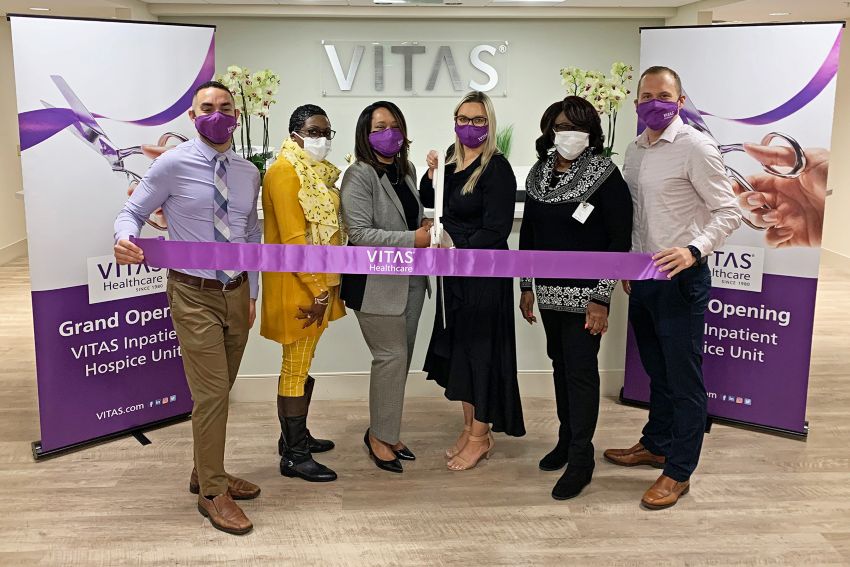 The group holds a purple ribbon for the ribbon cutting