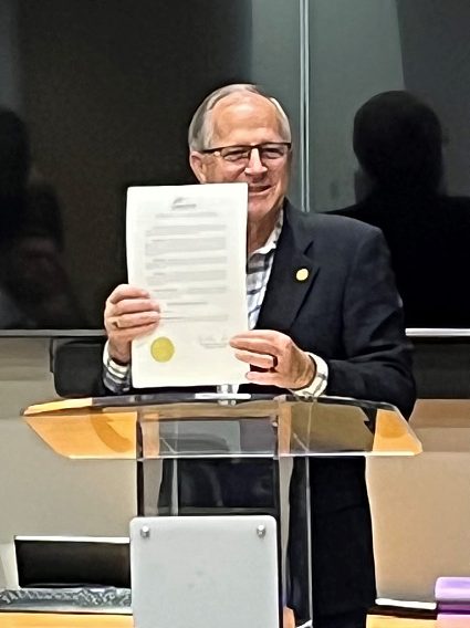 The mayor stands at the podium holding up the proclamation