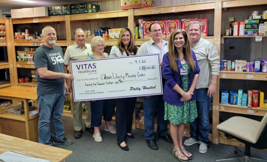The group poses with a ceremonial oversized check inside the food pantry