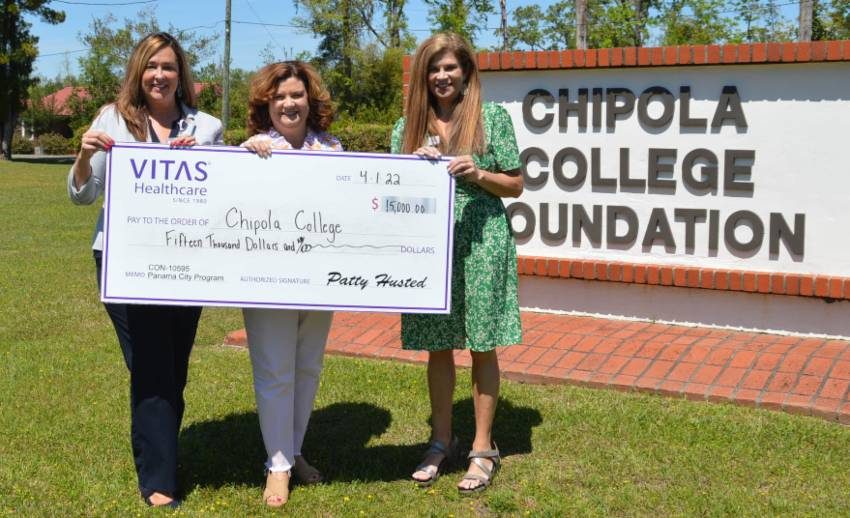 Three people hold a ceremonial oversized check near the sign for the Chipola College Foundation
