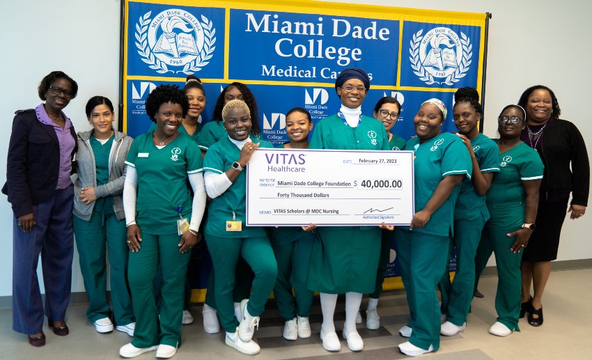 The group poses in front of a Miami-Dade College banner with a ceremonial oversized check