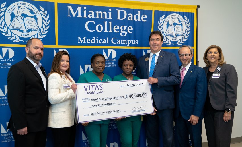The group poses in front of a Miami-Dade College banner with a ceremonial oversized check