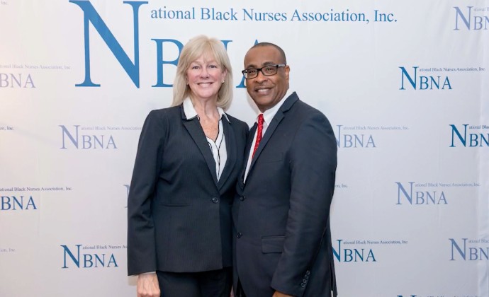 Two people posed in front of an NBNA banner