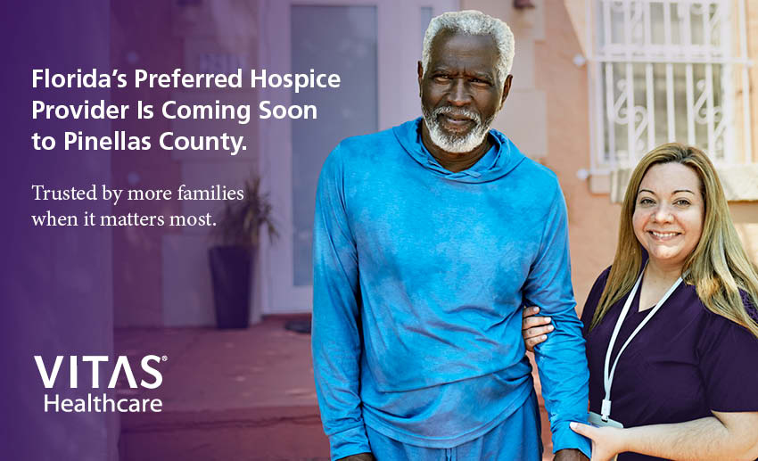 A clinician in purple scrubs holds the arm of an older male patient
