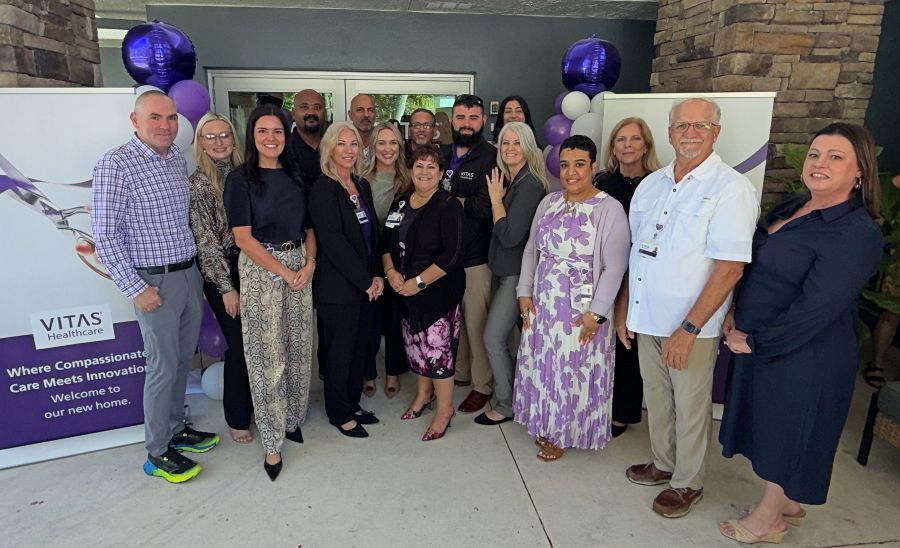 A group of people poses in front of a front entrance with balloons and banners