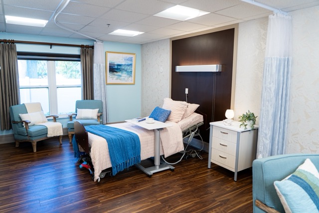 A patient room comfortably appointed with hospital bed, guest seating and bright windows