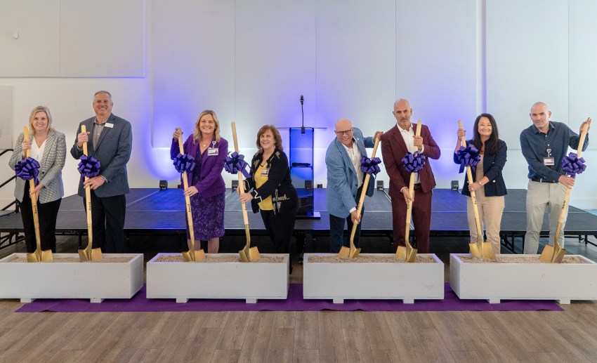 Eight people pose with ceremonial shovels in boxes of dirt for the official groundbreaking ceremony
