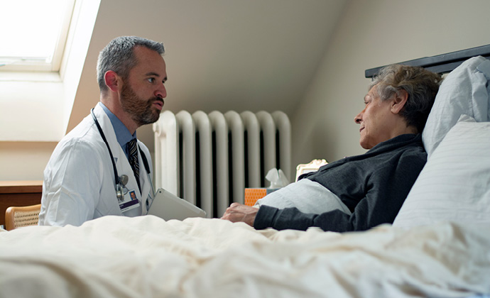A patient lies in bed at home and talks with a VITAS physician
