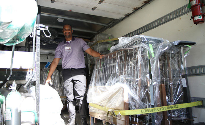 VITAS team member stands in the cargo area of a home medical equipment delivery truck that's loaded with a bed frame