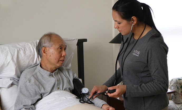 Una enfermera controla la presión arterial de un hombre sentado en su cama en casa