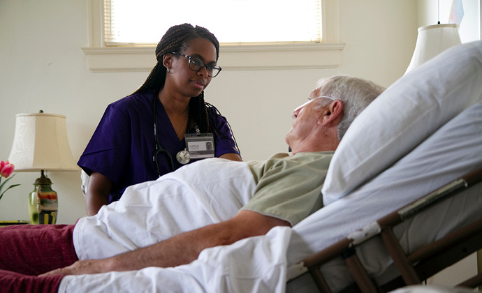 A male patient in bed at home talks with a VITAS nurse