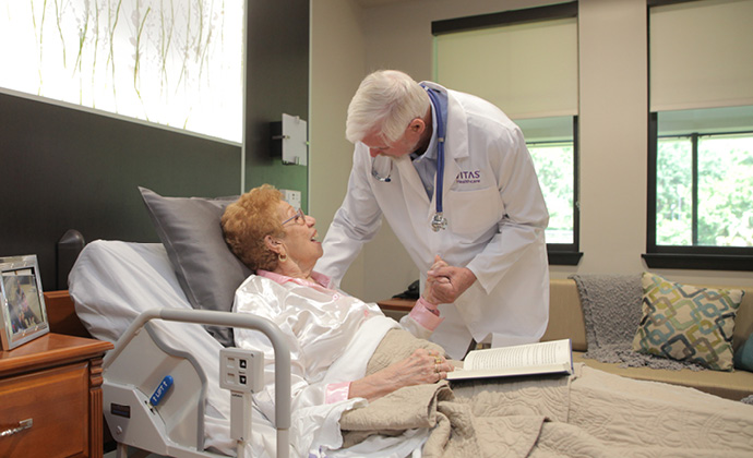 A physician talks with a woman who is lying in bed