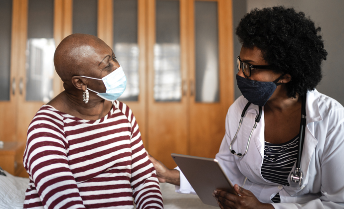 A physician and patient, both wearing masks, sit together in an office and have a conversation