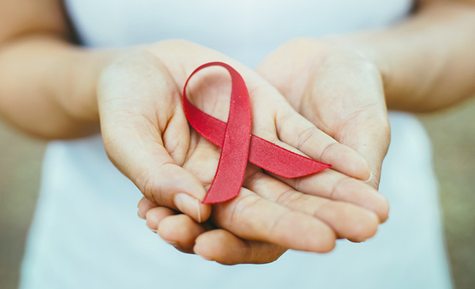 Una manos sostienen una cinta roja para concientizar sobre el SIDA