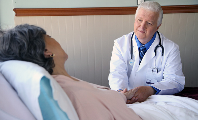 A woman lies in bed as a VITAS physician holds her hand