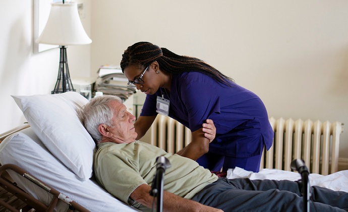 A VITAS team member helps a man sit up in bed