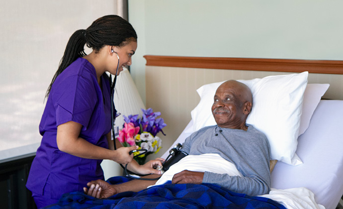 A VITAS team member uses a stethoscope to check on a man lying in bed