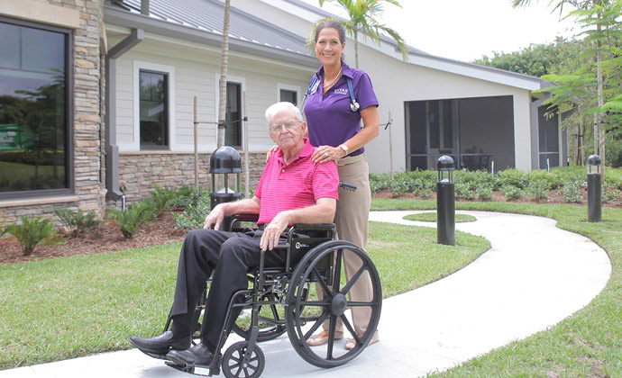 A man using a wheelchair on an outside path receives help from a VITAS team member