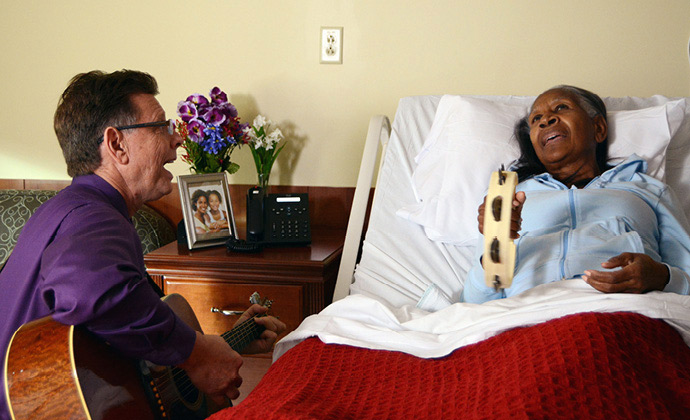 Một chuyên gia trị liệu bằng âm nhạc của VITAS chơi ghi-ta ở cạnh giường bệnh nhân, người đang chơi trống lục lạc.