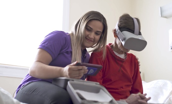 A VITAS team member sits next to a patient using a virtual reality headset