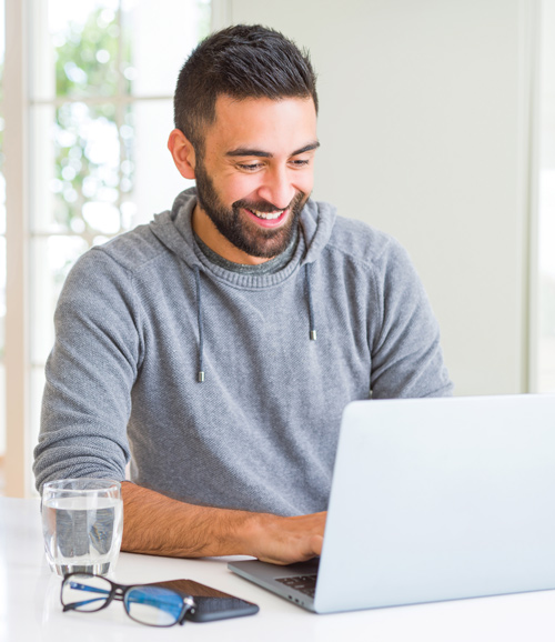 Un hombre sonríe mientras trabaja en una laptop
