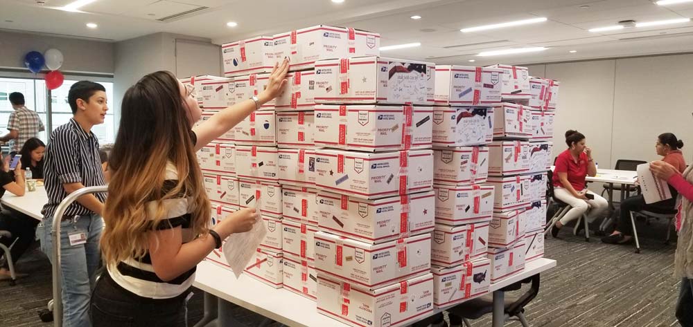 A VITAS team member inspects dozens of boxes with care packages stacked neatly on a conference room table