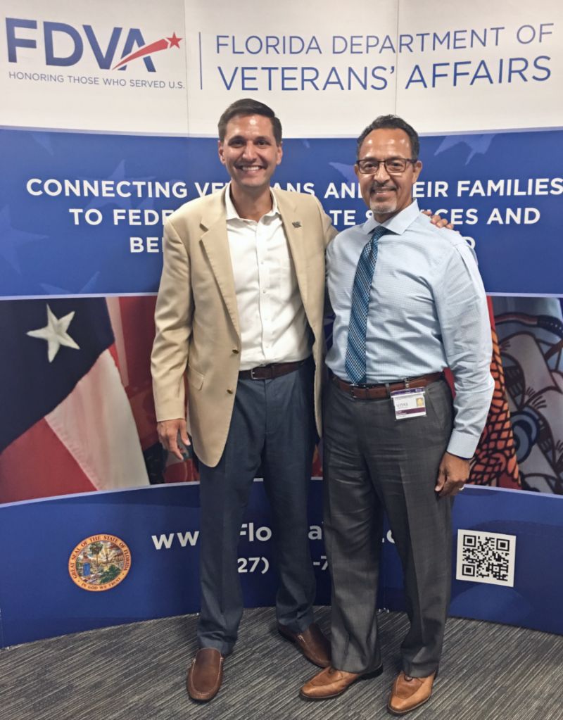The two men stand for a photo in front of a Florida Department of Veterans Affairs banner