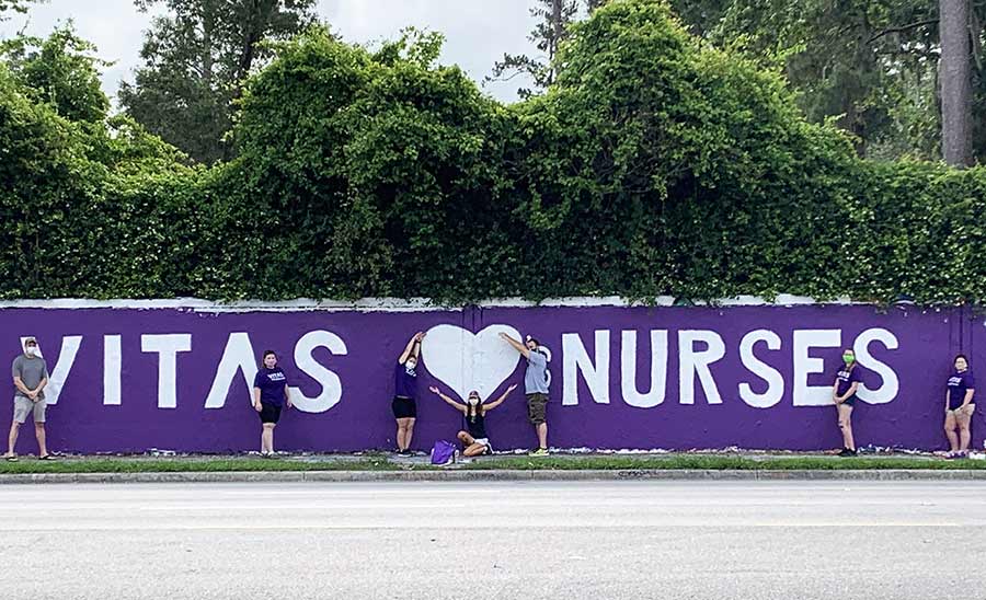 The artists pose with the completed mural, which has a purple background and white letters