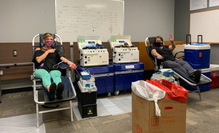 Two VITAS employees wave hello as they donate blood at the program office