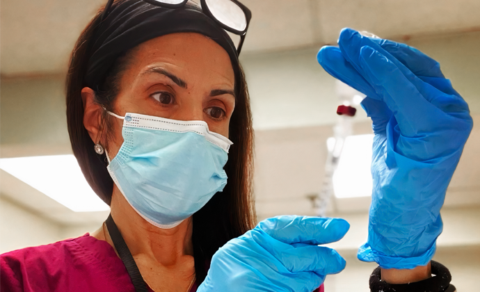 Denise Papagoda, wearing scrubs and a mask, fills a syringe with liquid.